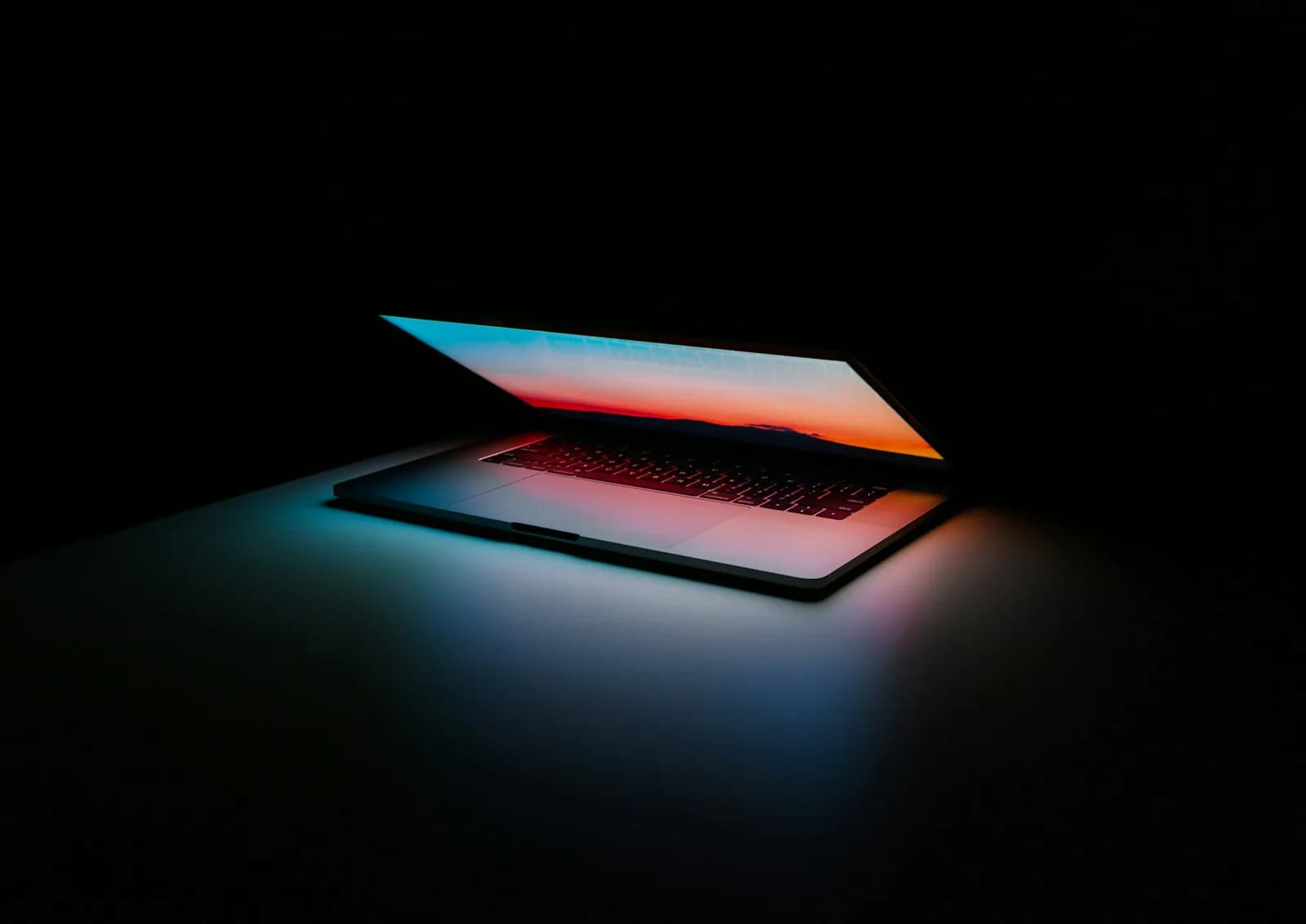 A laptop with its lid almost closed on a dark table