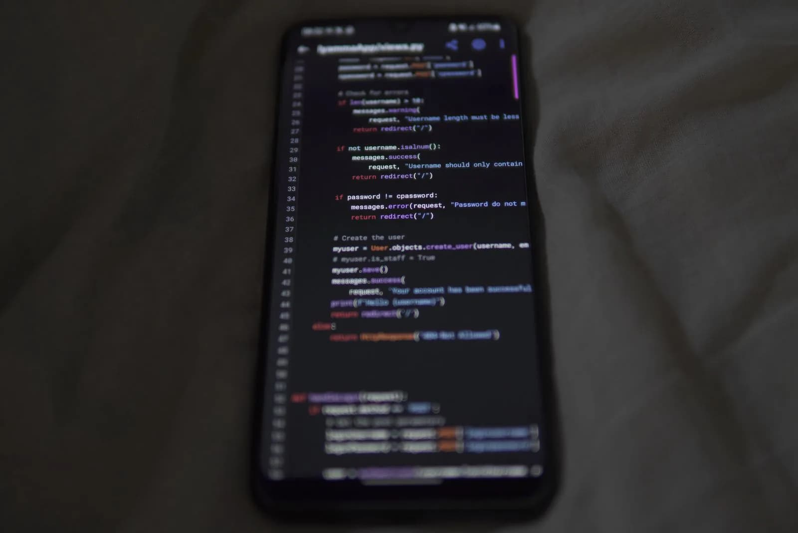 A phone with code on its screen, lying on a grey sheet